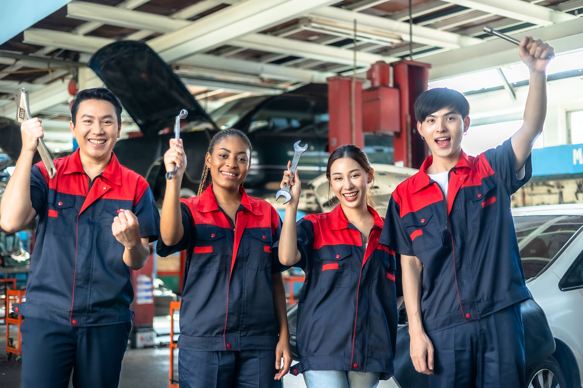 Four car mechanics cheering together with tools in their hands
