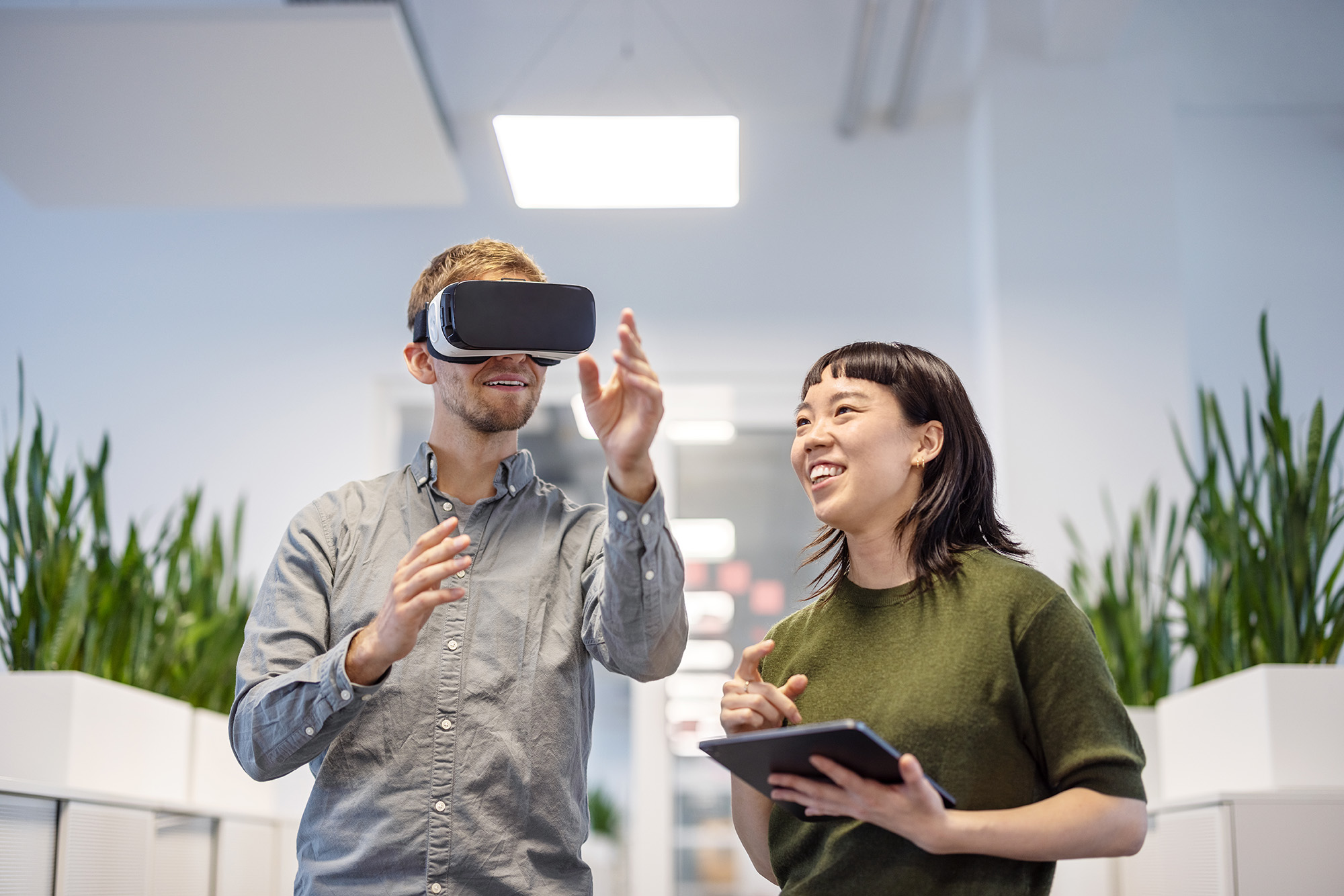 Young man using VR glasses with female colleague holding digital tablet at office